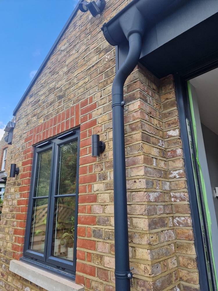 Matched-in brickwork detail with grey window and downpipe on completed extension