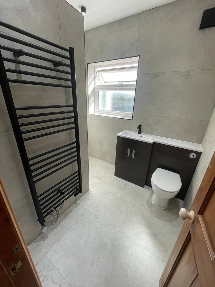 Modern grey bathroom with vanity unit, WC and black ladder radiator by DR Construction