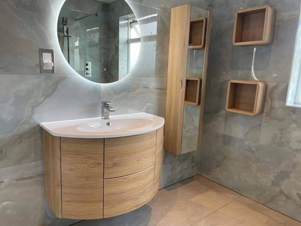 Bathroom with curved wooden vanity, round LED mirror and marble-effect tiling in Northwood