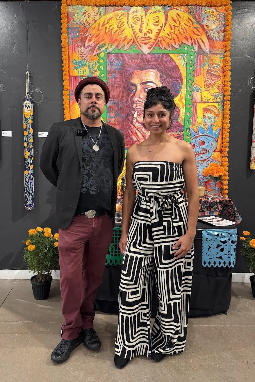Artists Francisco Franco and Marissa Zamudio at Create Gallery and Frames during their October exhibition, standing in front of colorful artwork framed with orange marigolds