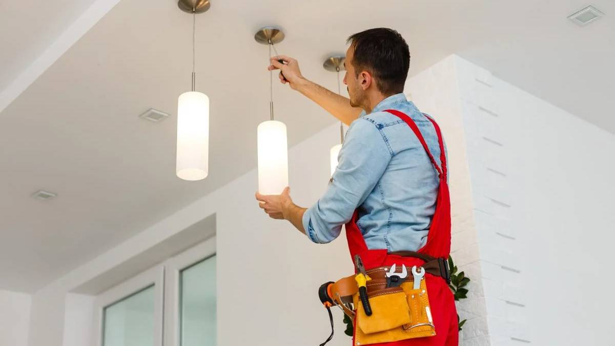 Residential electrician or HVAC technician wearing a tool belt and inspecting indoor lighting fixtures.
