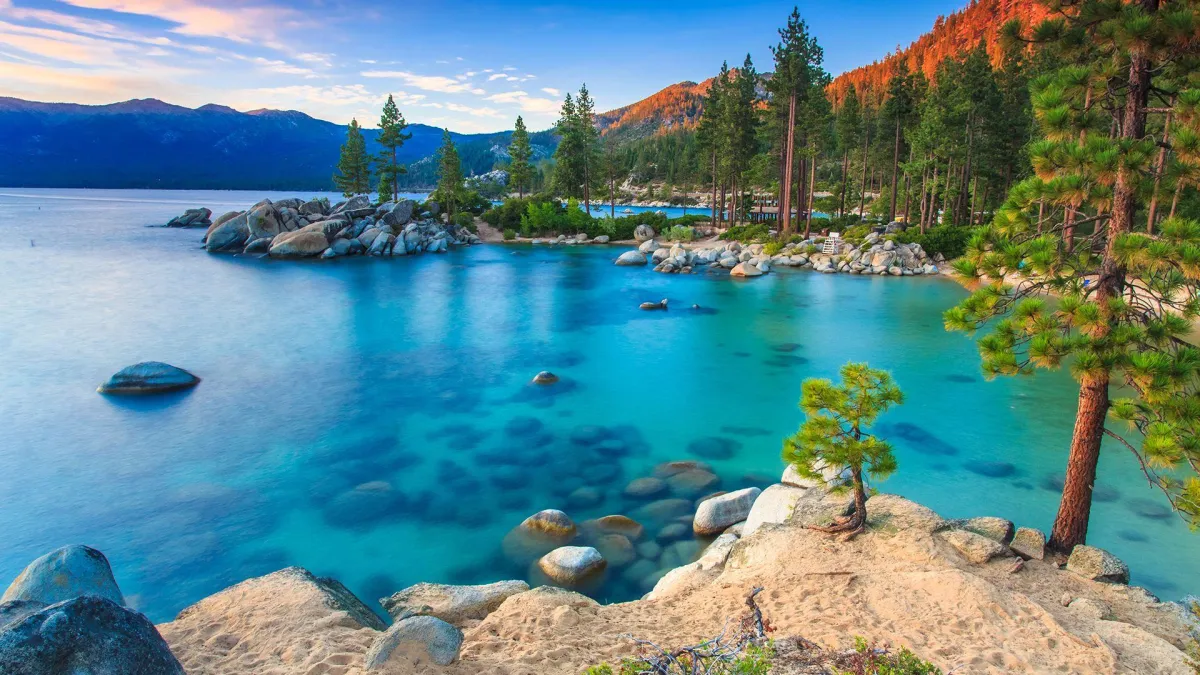 Vibrant shoreline of Sand Harbor State Park, Lake Tahoe with rugged, rocky outcroppings pushing into teal and aquamarine, clear waters with blue mountains in the background and redwoods dappling the shoreline