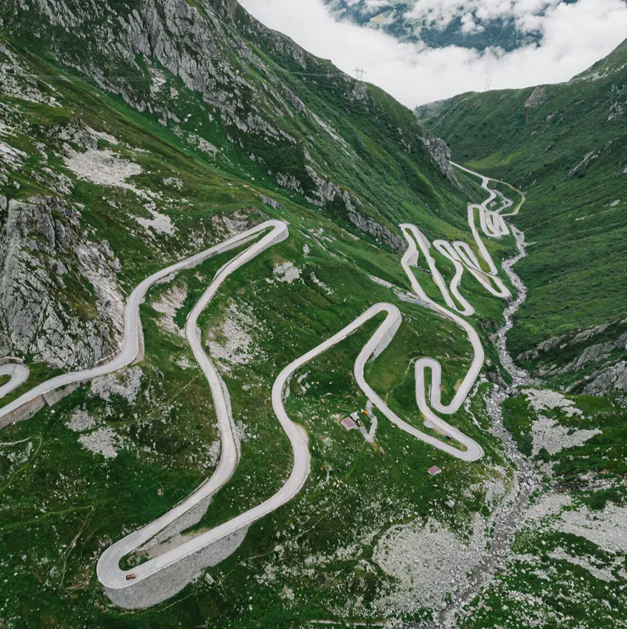 Aerial view of Katakluz Pass, a squiggly, gray road looping again and again on hairpin turns up the green but rocky, steep slopes