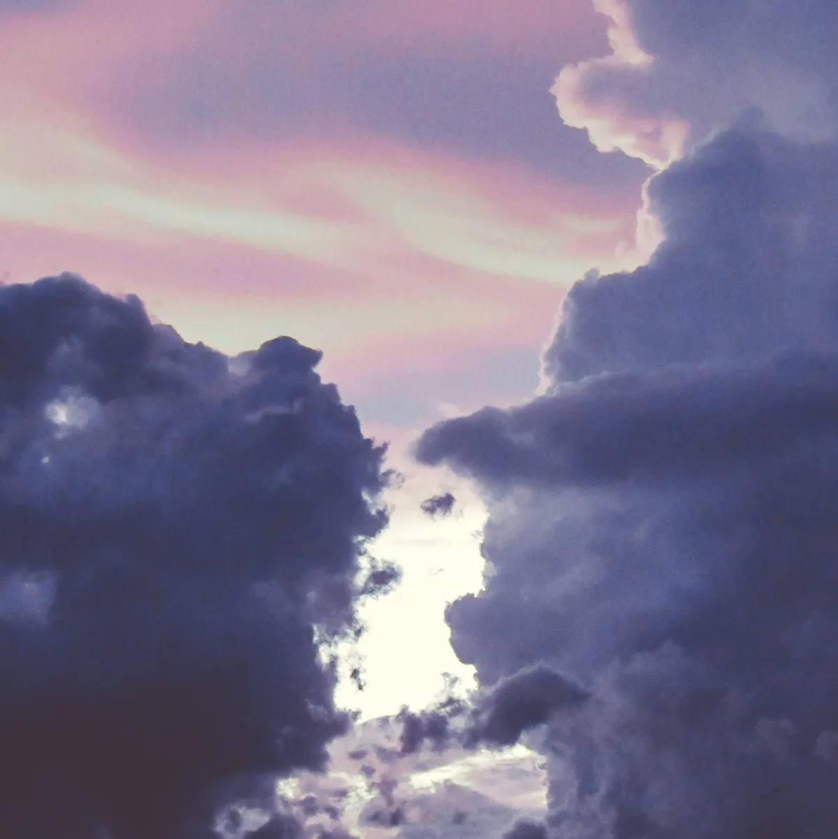 Purply clouds parting in the heaven to reveal distant light and graying hues of pinks and purples