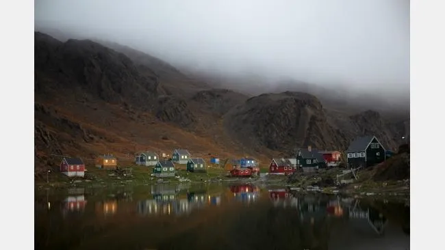 Tranquil Skoto Lake with a village dappling its far bank, and foreboding hills with heavy, low clouds creeping in