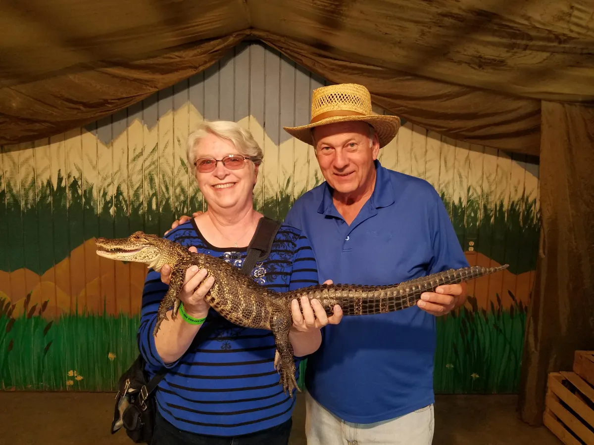 C. S. Fitzpatrick and her husband smiling while holding a small alligator in their outstretched hands while at an alligator farm in Colorado