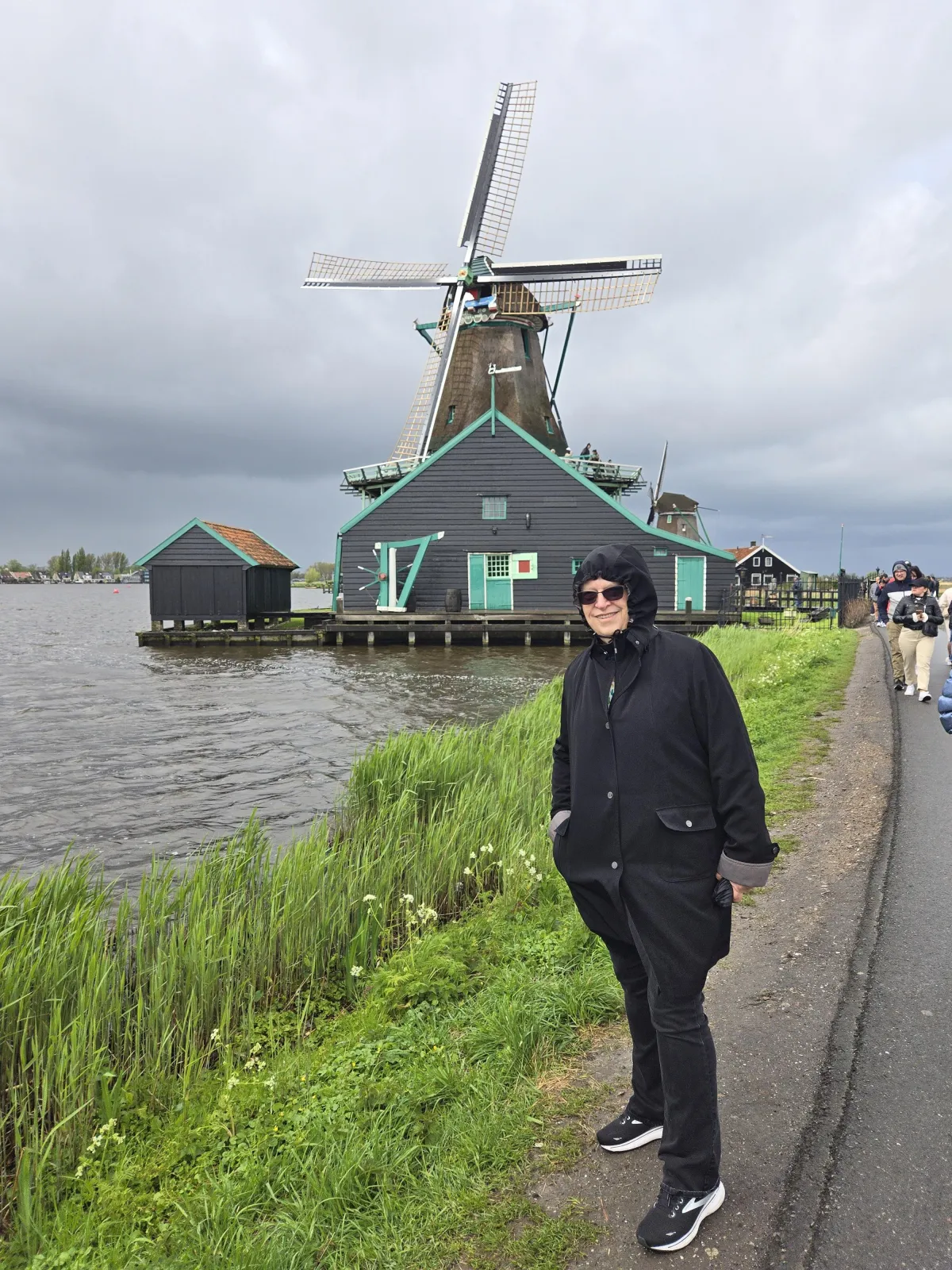 C. S. Fitzpatrick standing before a windwill at the water's edge on a stormy day in Holland with a grin on her face despite stormy skies and gray waters