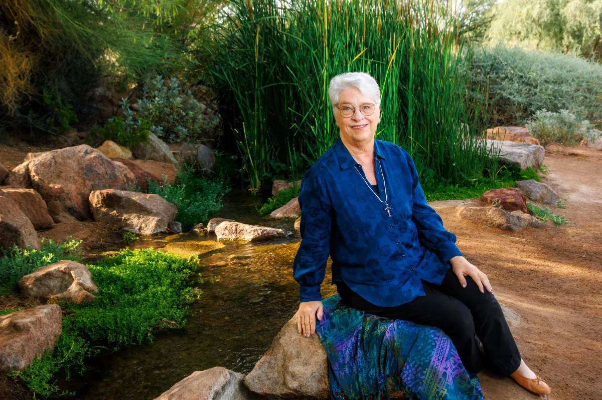 C. S. Fitzpatrick sitting on a sarong draped over a rock beside a tranquil pool of water surrounded by red rocks and vibrant green foliage