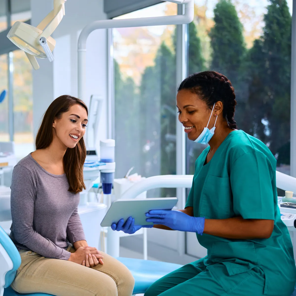 Dental assistant sitting down with patient holding a tablet and showing information