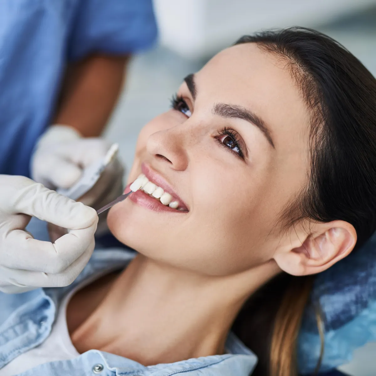 Woman laying down and dentist holding a set of teeth with different shades of color