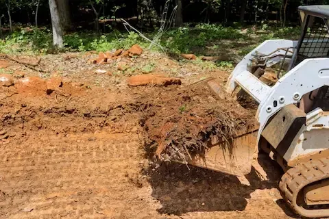 Skid steer drags a mat of roots and soil across a cleared land-clearing site