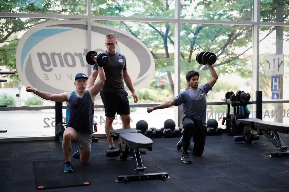 Two members kneeling with a personal training coaching them through an overhead press