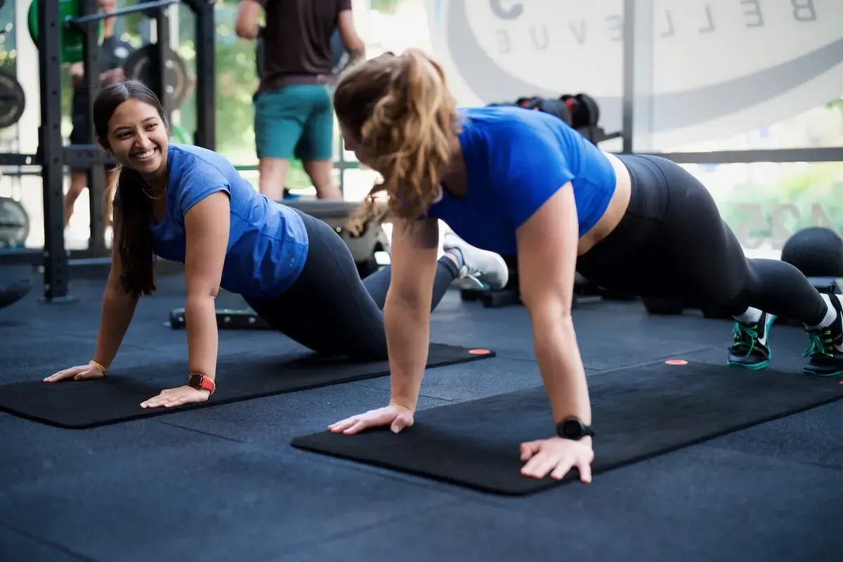Two members wearing blue shirts in a pushup position, smiling during their workout