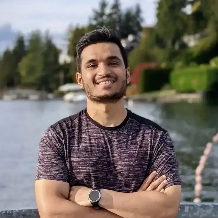 A member posing for a photo in front of a lake with his arms crossed and smiling.
