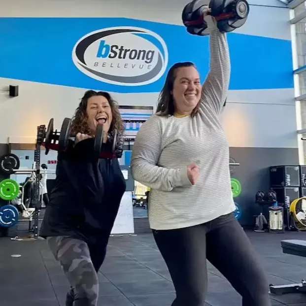Two members in the gym holding dumbells with smiles. 
