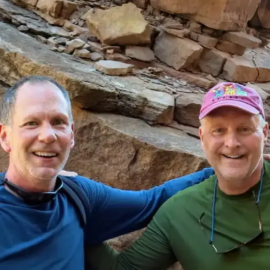 Two members in front of rocks with their arms around each other and smiling. 