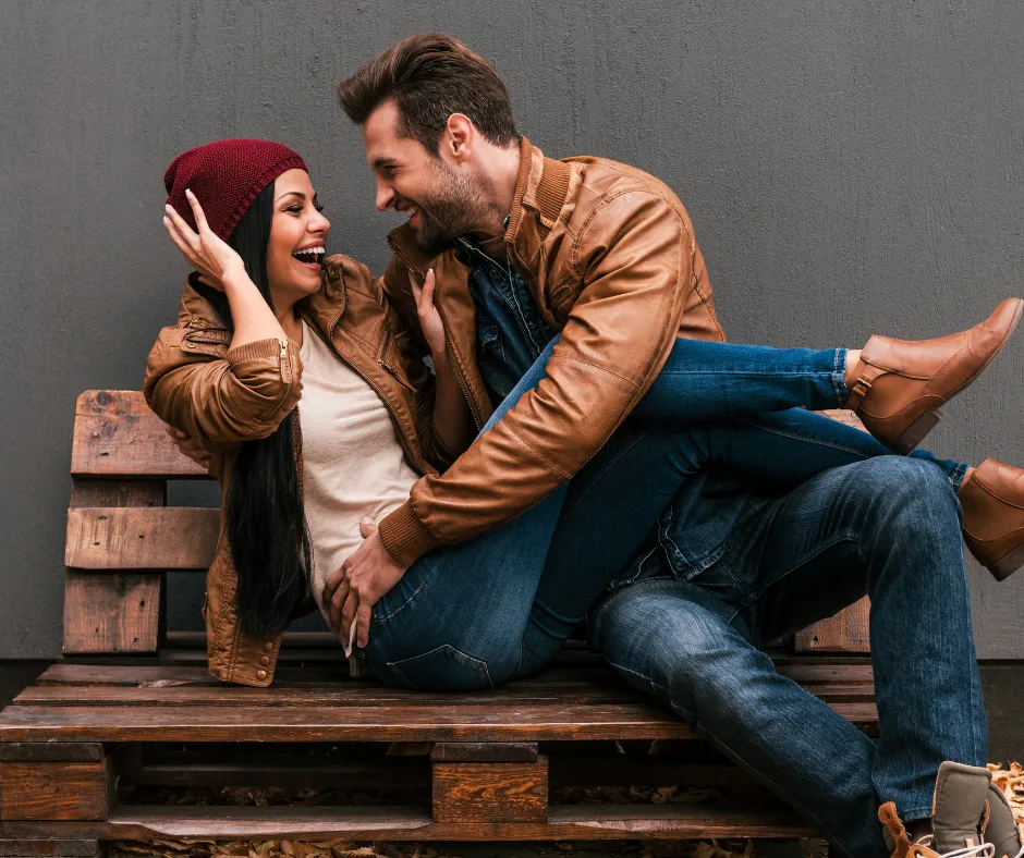 A playful couple sitting on a bench.