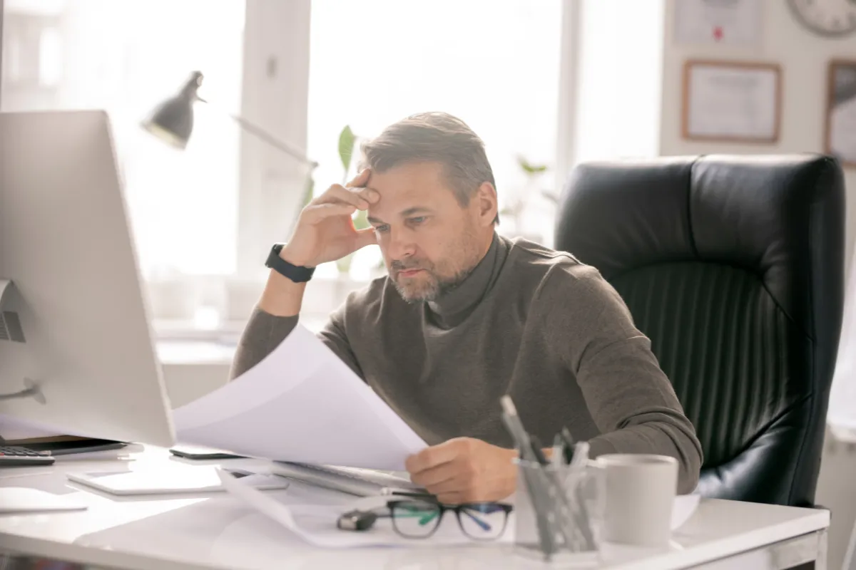 Stressed professional reviewing paperwork at an office desk. 