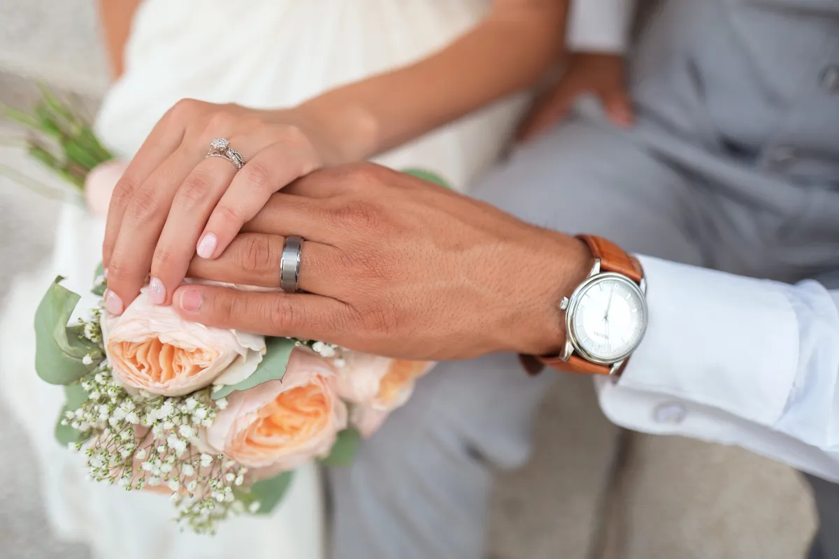 Newlywed couple holding hands over a wedding bouquet during a romantic moment.