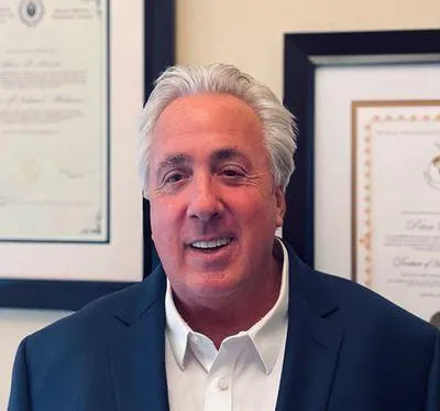 Photo of Dr. Peter Amato, smiling with several accreditations hanging on the wall behind him.  