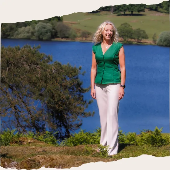 Sally MacDonald standing outdoors by a lake and trees, portrait
