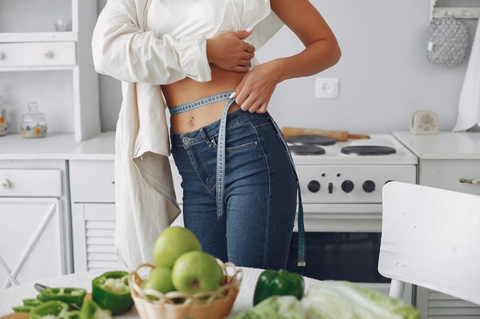 Fit women measuring her waist to show fitness