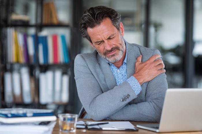 Office Man in Tucson, AZ with Shoulder Pain squeezing his shoulder