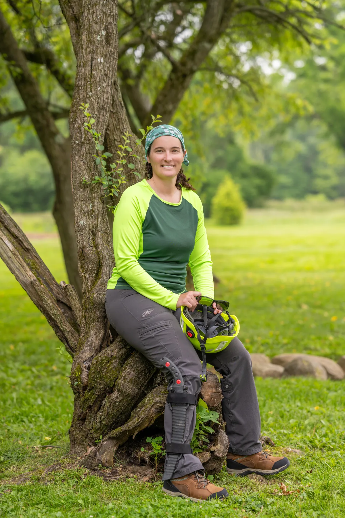 Master arborist in trekking tights and long-sleeved shirt, taking a break by a tree.
