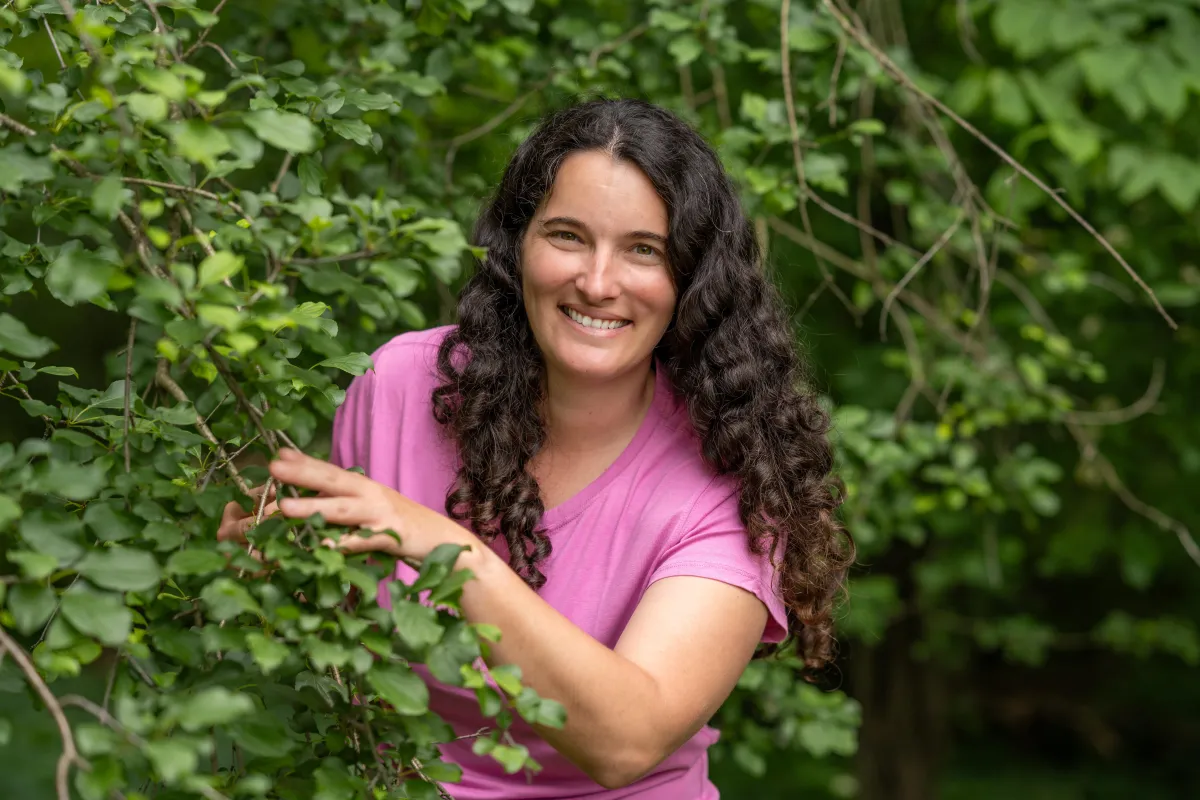Tina L Graver, a master arborist, smiling among lush green foliage.