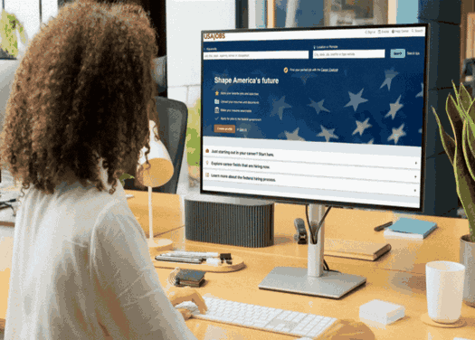 Professional woman browsing the USAJOBS federal hiring website on a desktop monitor.