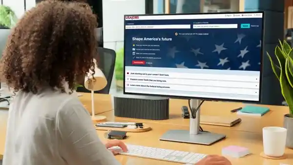Professional woman browsing the USAJOBS federal hiring website on a desktop monitor.