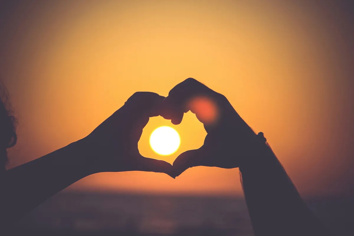 Two hands forming a heart around the setting sun