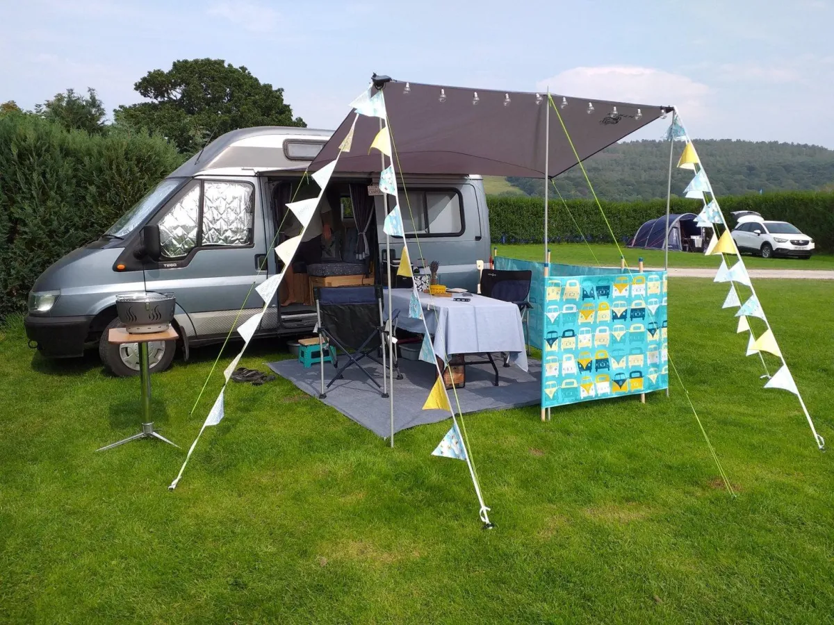A gre campervan with sun canopy and blue and yelow bunting