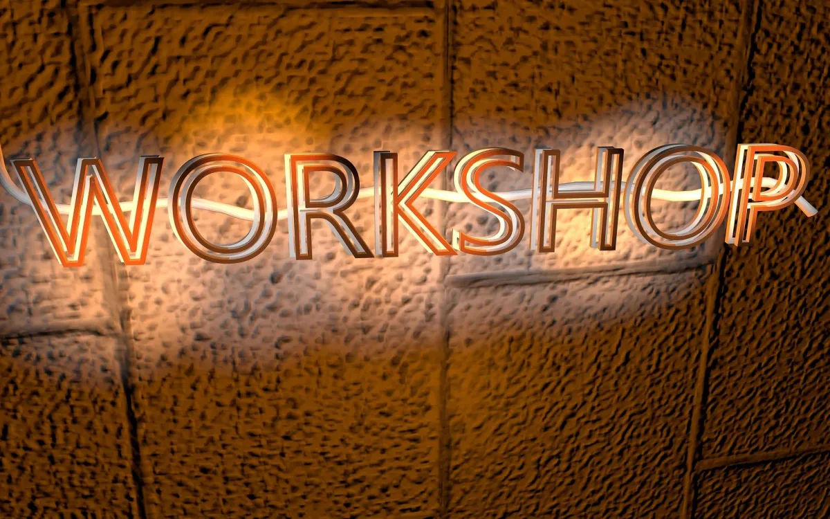 Neon-lit 'WORKSHOP' text glowing against a textured brick wall background, symbolizing Vee Khuu's dynamic AI Trainer workshops designed to empower business leaders with practical AI applications.