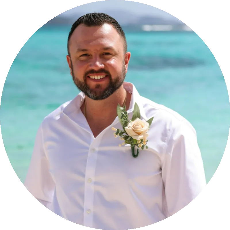 Smiling man in a white shirt with a floral boutonniere, standing by the water, showcasing professionalism and approachability, representing Bulldog Concrete's commitment to quality and customer service partnership with Bulldog Concrete