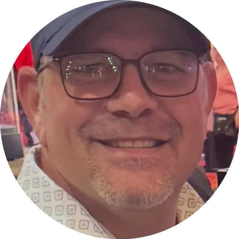 Smiling man wearing glasses and a cap, representing leadership in the concrete and excavation industry.