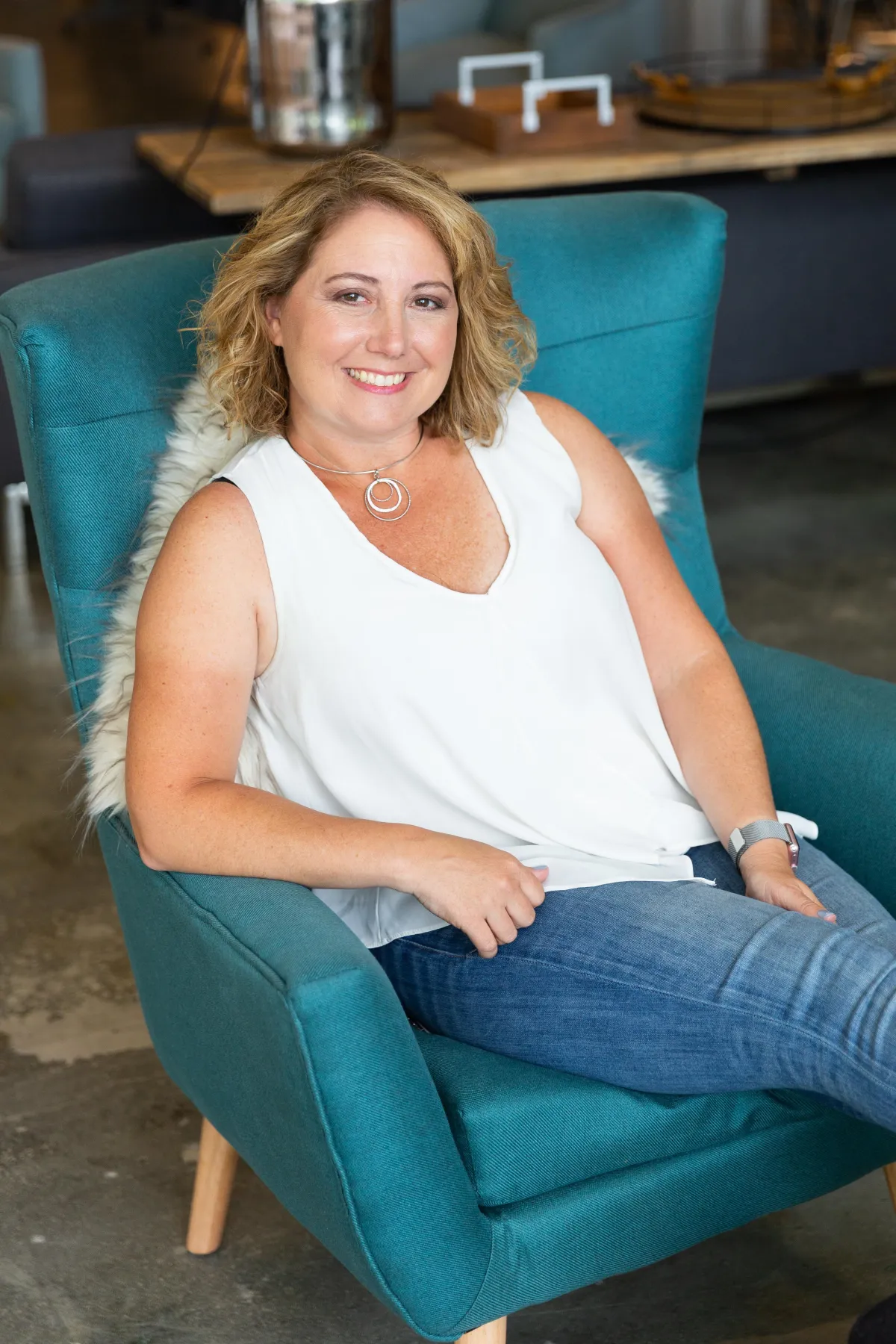 Kristen Arnold, Fractional COO and leadership strategist, smiling while seated in a teal chair, representing calm, confident business leadership.