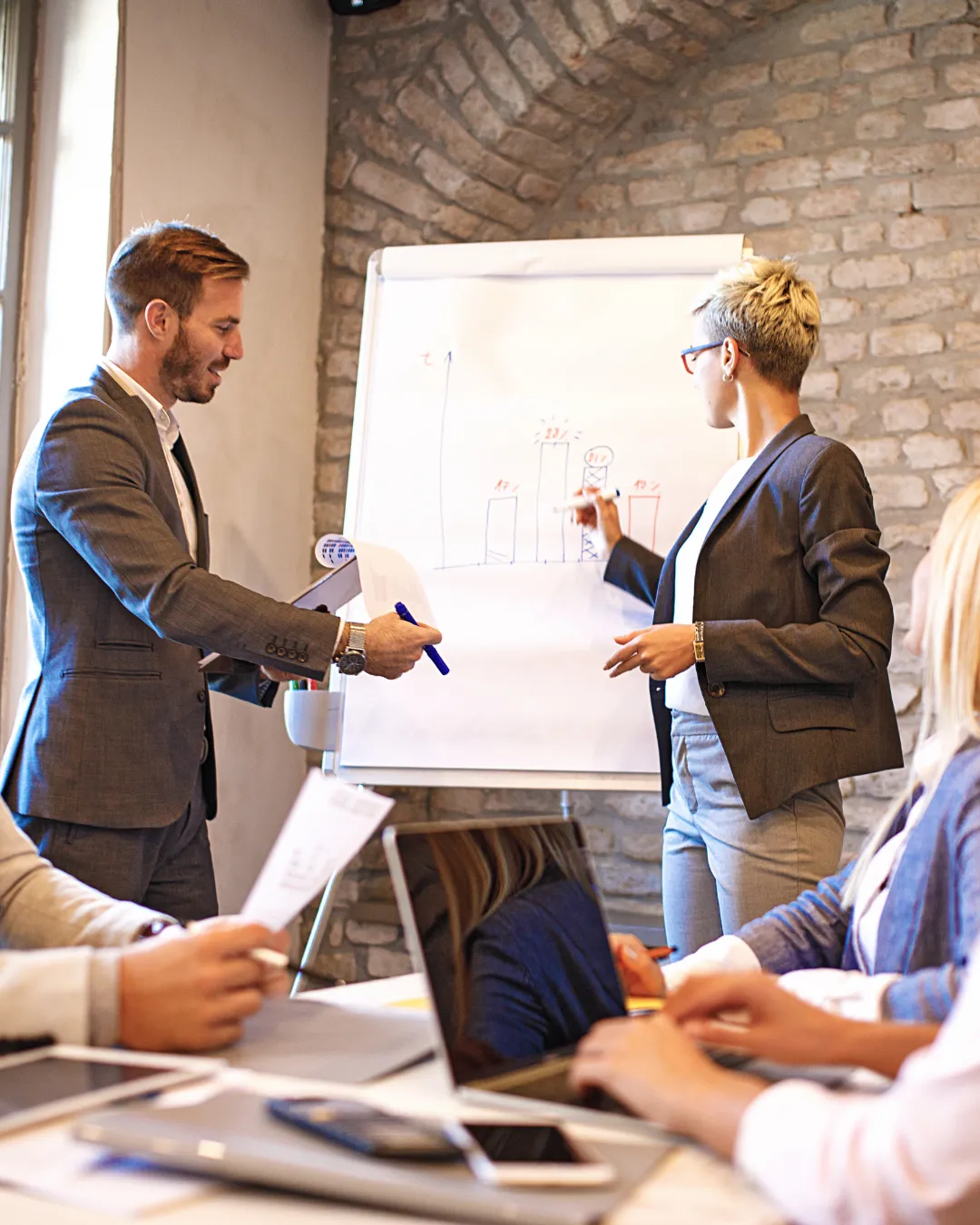 Two business leaders presenting operational strategies to their team, representing Kristen Arnold’s Fractional COO service that stabilizes execution and aligns leadership.