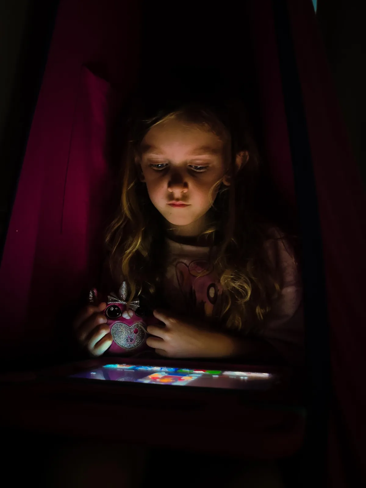 Portrait of a young girl illuminated by the soft glow of a tablet screen in a dark room, holding a sparkly toy. The image captures a quiet, introspective moment, showcasing Drake Nix’s ability to convey mood and atmosphere in low-light photography.