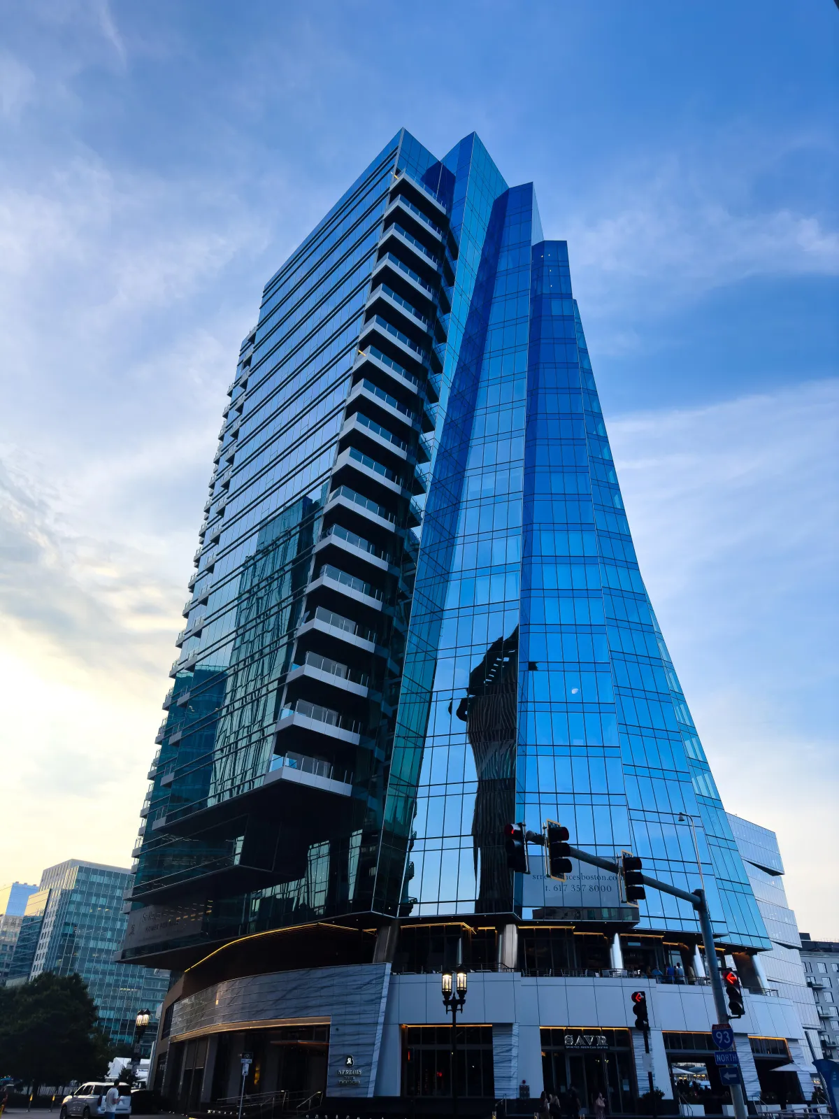 Modern glass skyscraper against a clear sky, showcasing reflective architecture and sleek, angular design. The building's mirrored surface captures nearby structures, highlighting Drake Nix’s architectural photography skills in capturing urban aesthetics and reflections.