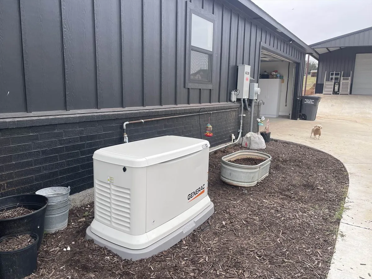 A standby generator installed outside a residential home, positioned next to utility meters and a gravel pathway