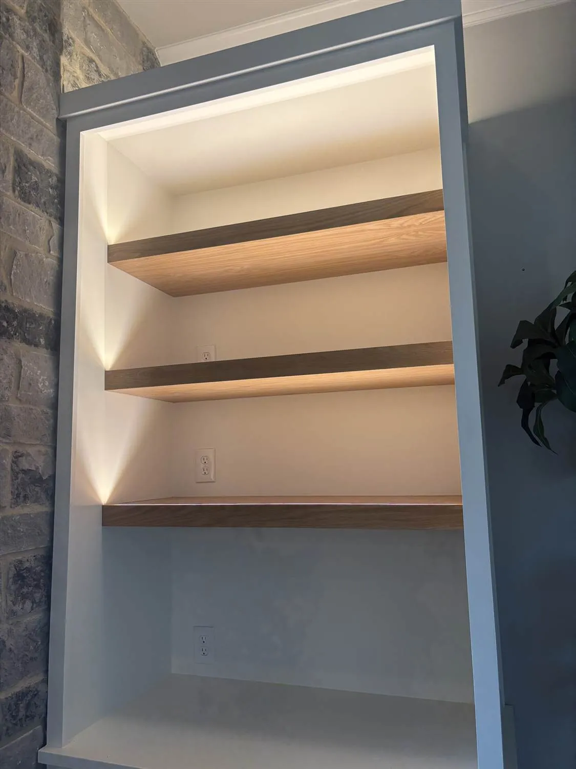 Close-up view of wooden shelves set into a wall alcove, featuring warm LED strip lighting installed underneath each shelf.