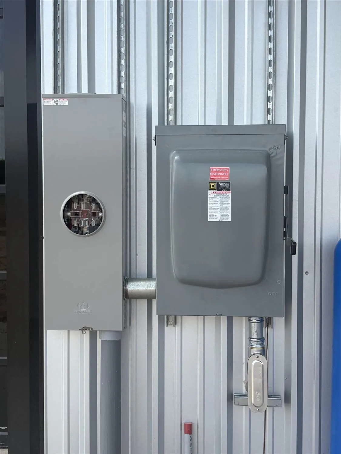 Two grey electrical service panels mounted side-by-side on a corrugated metal interior wall.
