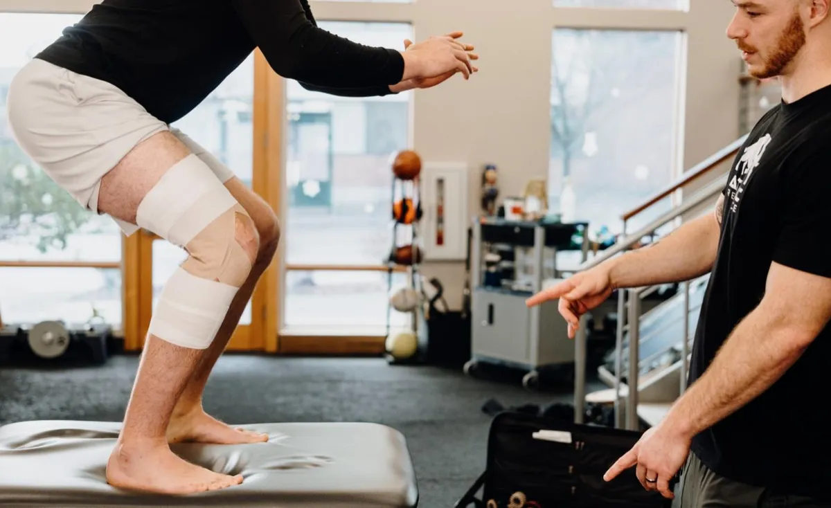 Clinician coaching an athlete with a taped knee through a squat