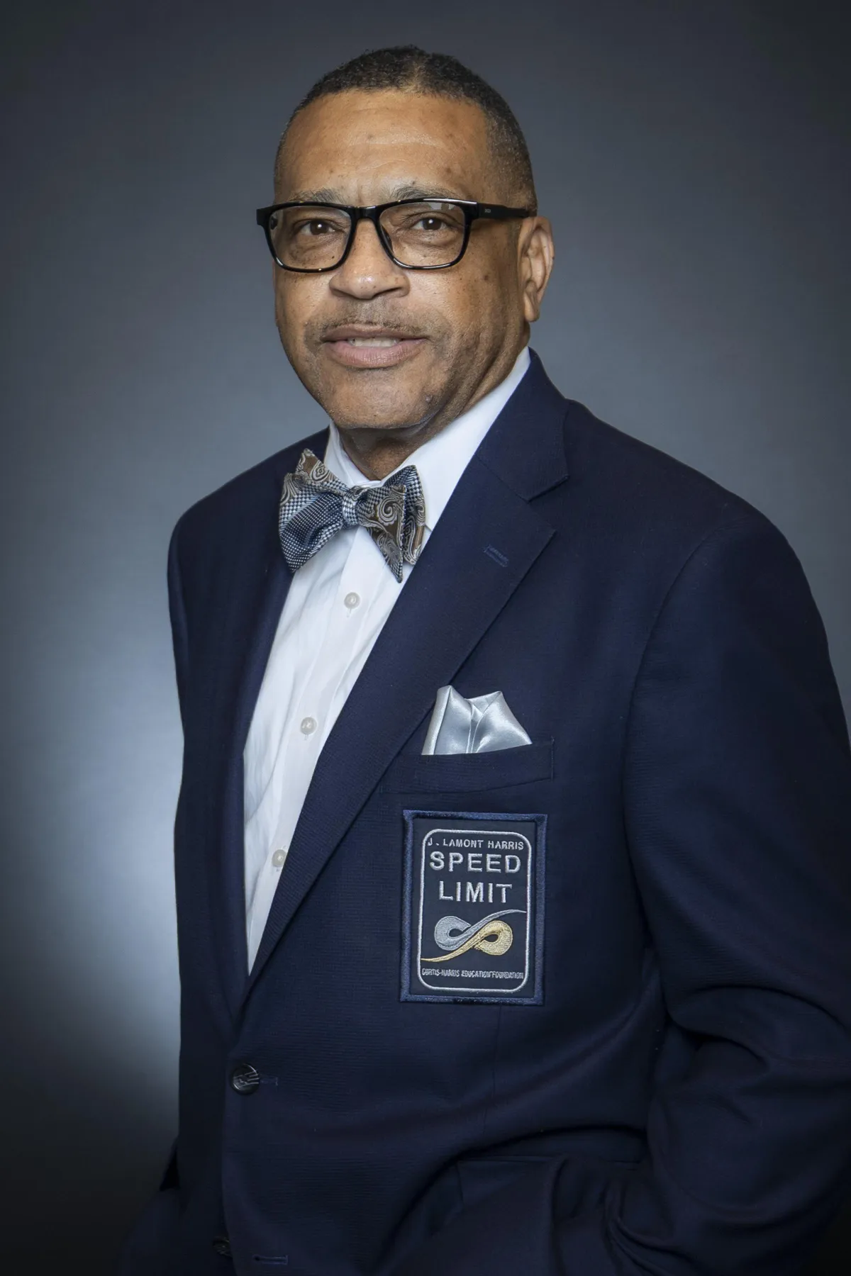 A formal portrait of J. Lamont Harris, an African-American man in a tailored suit, standing confidently in a sunlit library with shelves of leadership books behind him. The setting exudes wisdom, tradition, and a commitment to lifelong learning.