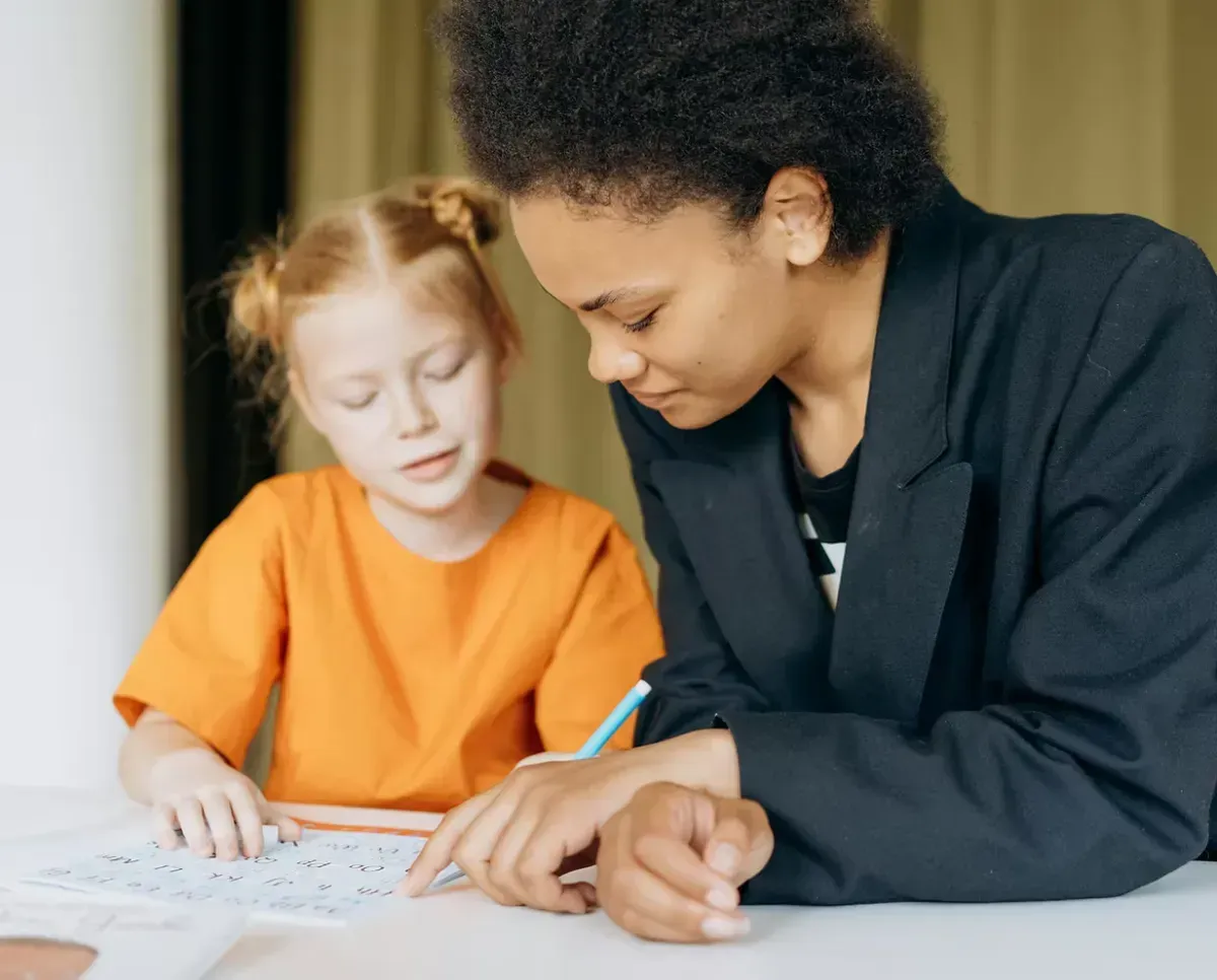 Teacher helping a young student with reading and writing activities during a one-on-one tutoring session.