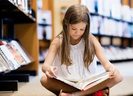 Young girl reading a book in a library to build literacy and reading comprehension with iReading Tutor