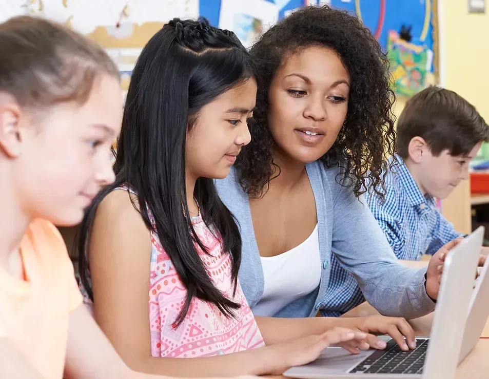 Teacher guiding elementary students through an interactive reading lesson using a laptop to build literacy and reading skills.