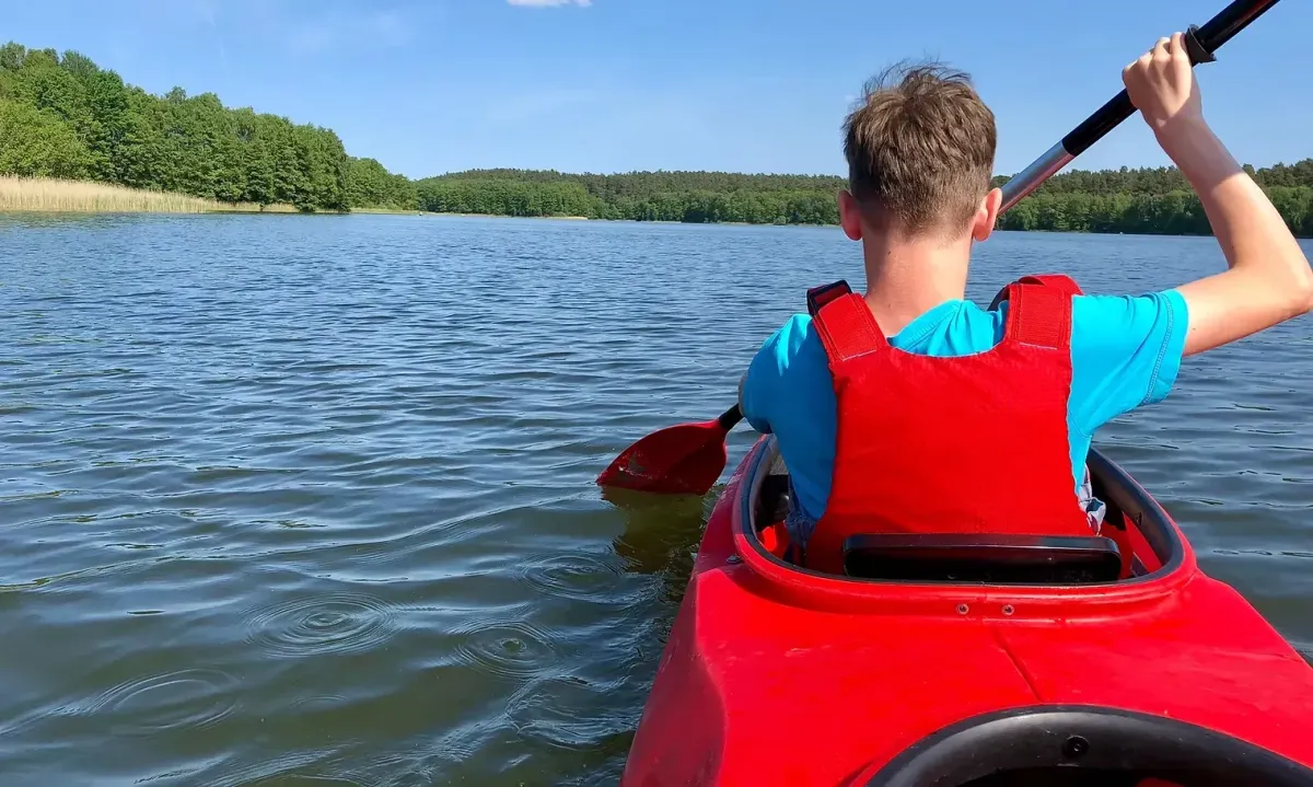 Student kayaking on a peaceful lake during the IReading Tutor summer program outdoor adventure.