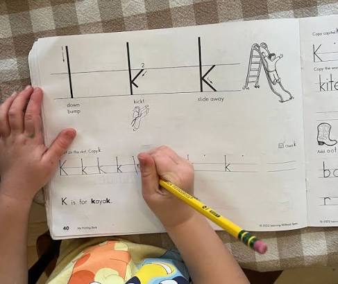 Close-up of a student's hand writing in a notebook during a reading and handwriting lesson with iReading Tutor.